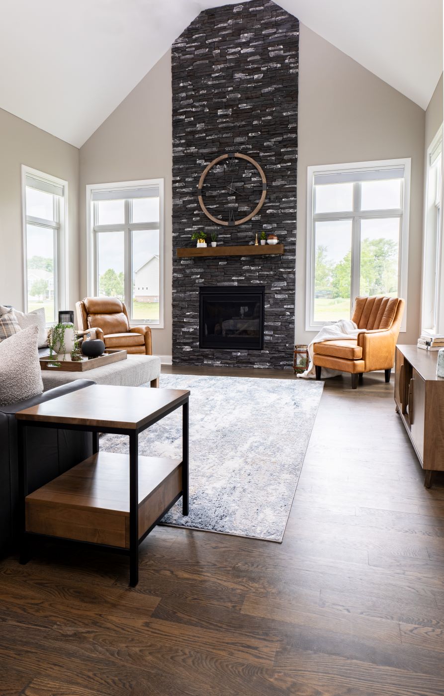 Two Vanderbilt Chairs sit in the corners of two large windows on either side of the room with a Dane End Table sitting next to a grey leather sofa