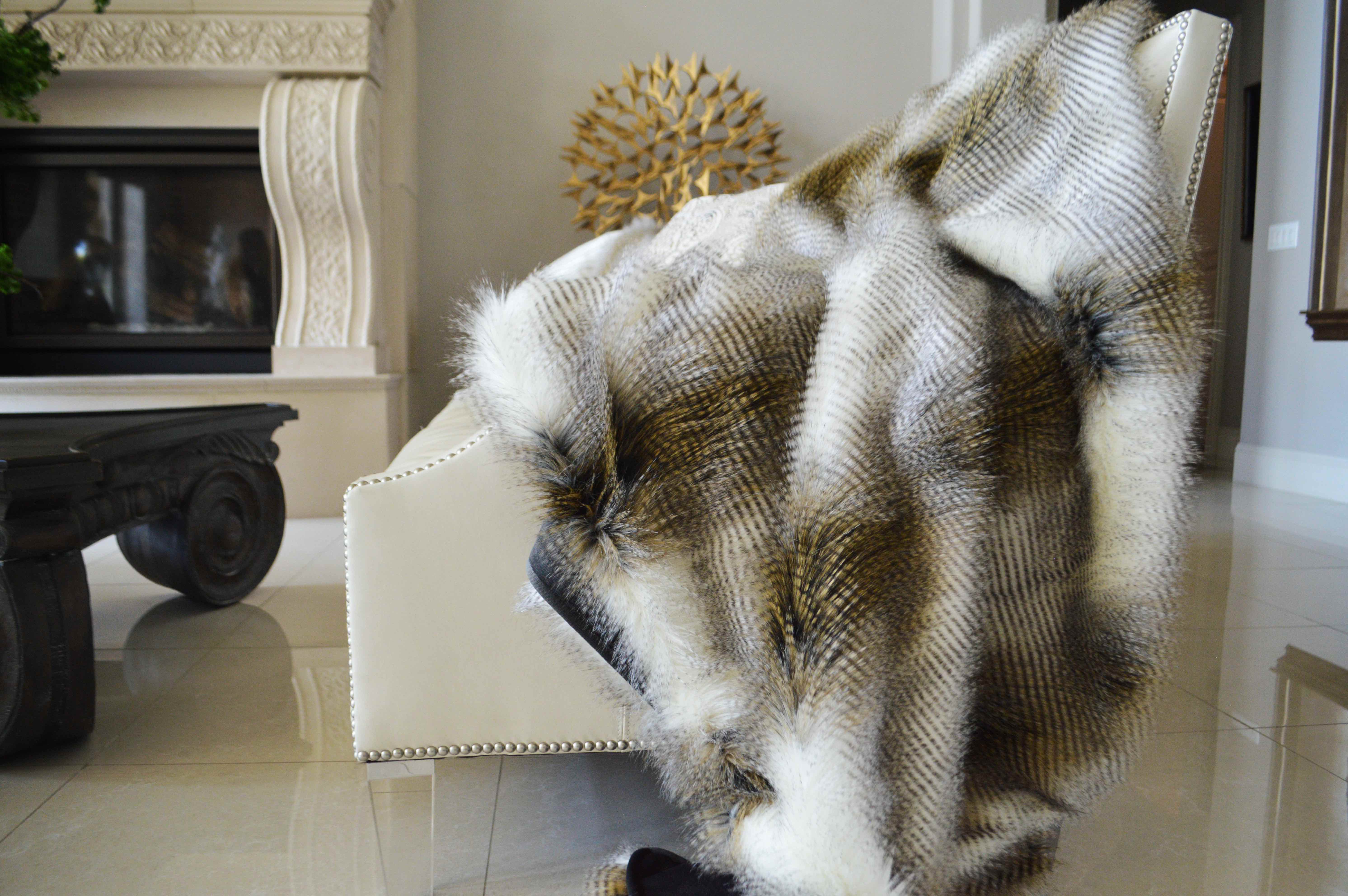 A white chair sits on a marble floor draped in a fuzzy faux animal skin blanket