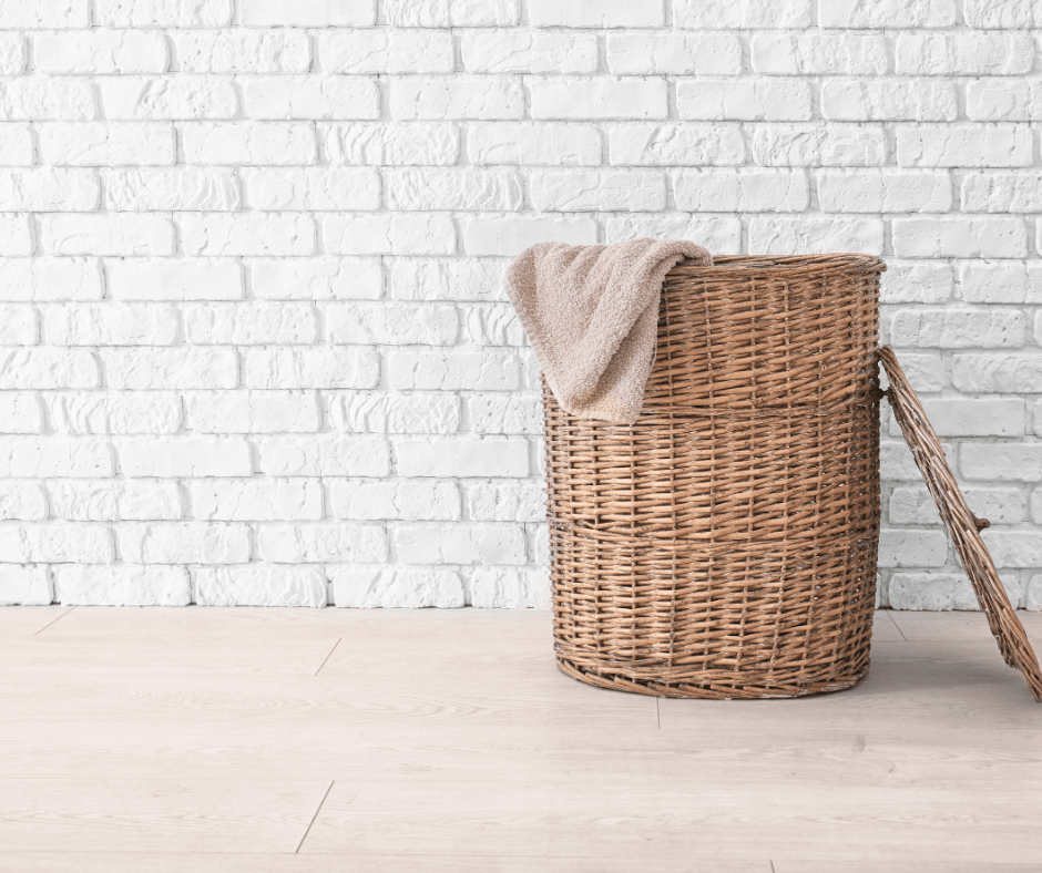 A wicker laundry basket with a towel hanging out sits against a white brick wall