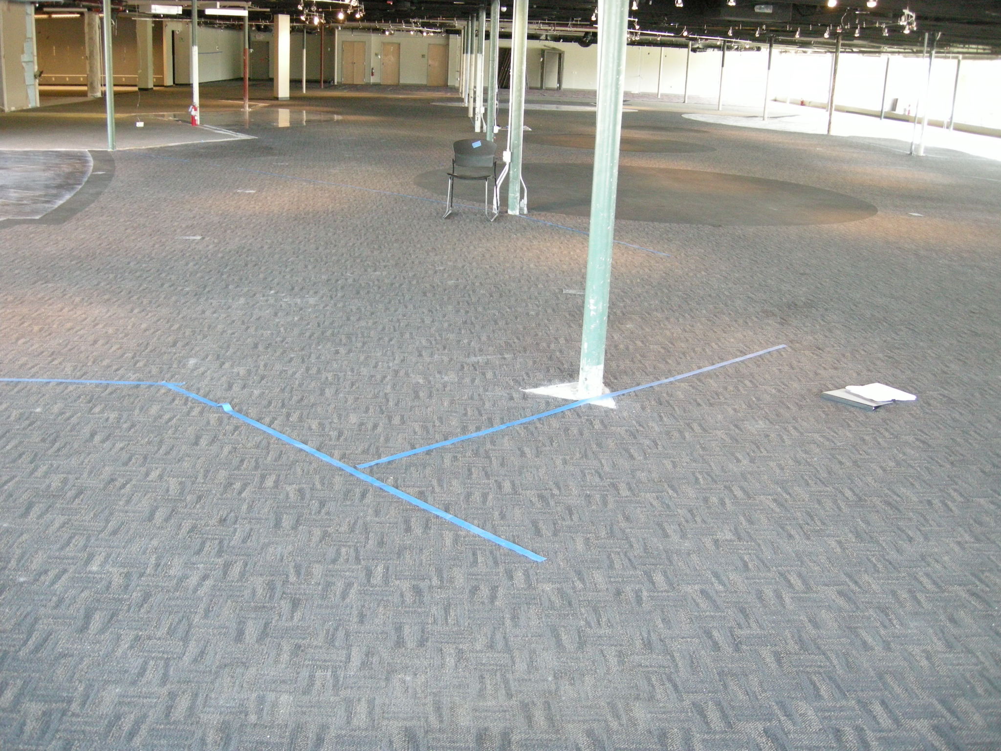 Another view of a furniture store under construction with exposed support pillars sitting in rows across the room and blue tape on the temporary carpet