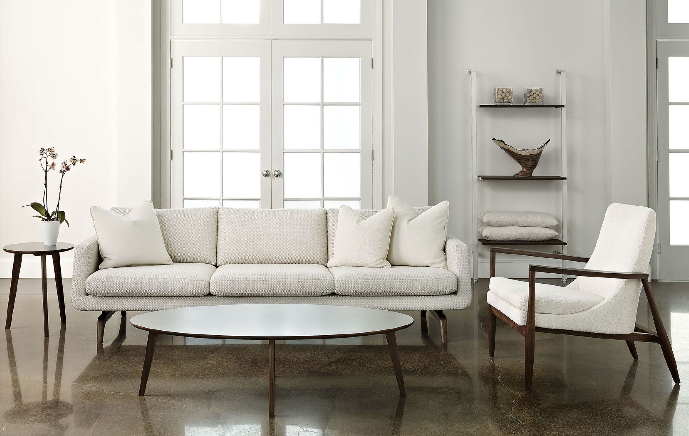 The Nash Sofa sits on a stone floor flanked by matching furniture in a white room with large windowed double doors