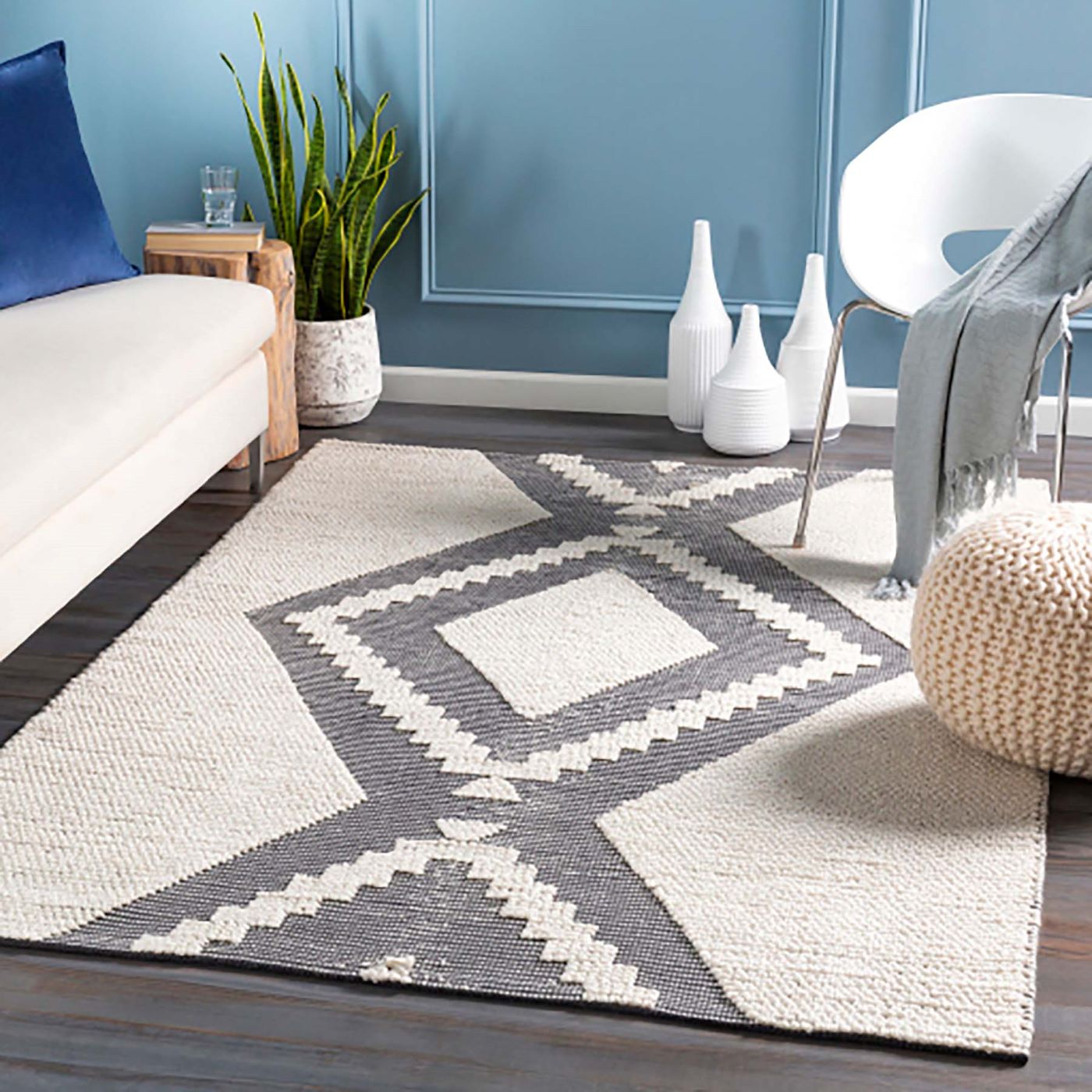 The SUAZA Rug in grey and white sits in a blue living room with decor resting around it