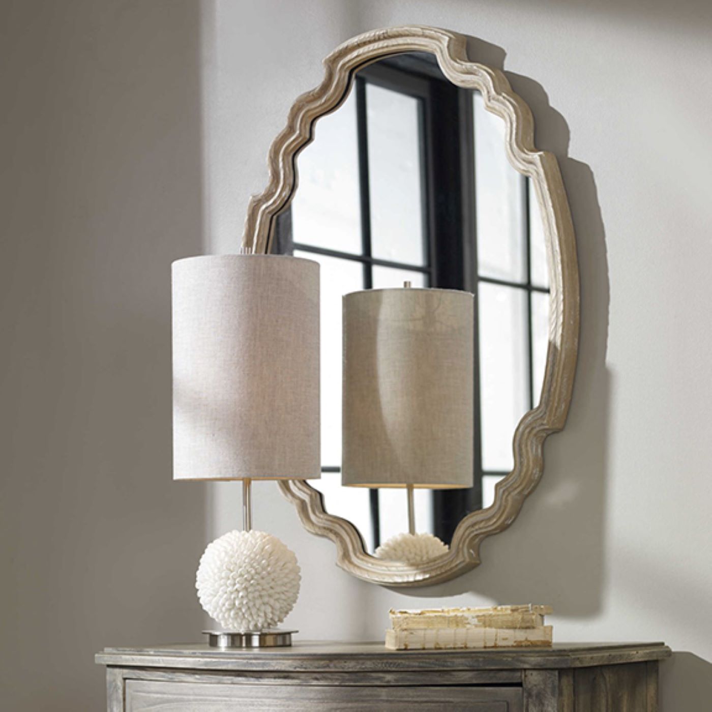 The UT14483 Wall Mirror hangs on a white wall above a chest of drawers that is topped with a stylish lamp